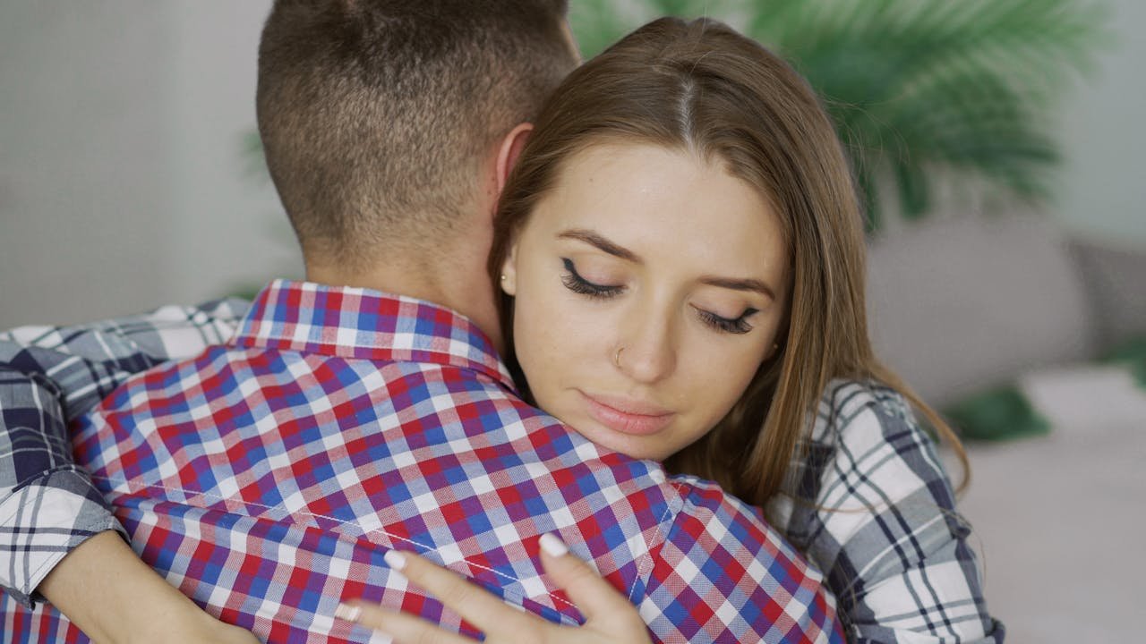 A young couple embraces indoors, expressing comfort and emotional support.
